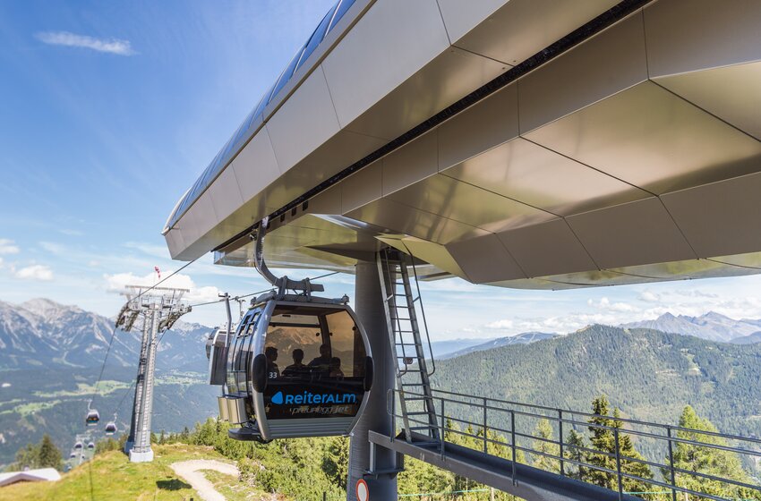 Preunegg Jet gondola at Reiteralm departs modern station, floating above green slopes with alpine panorama. | © Reiteralm Bergbahnen GmbH & Co.KG