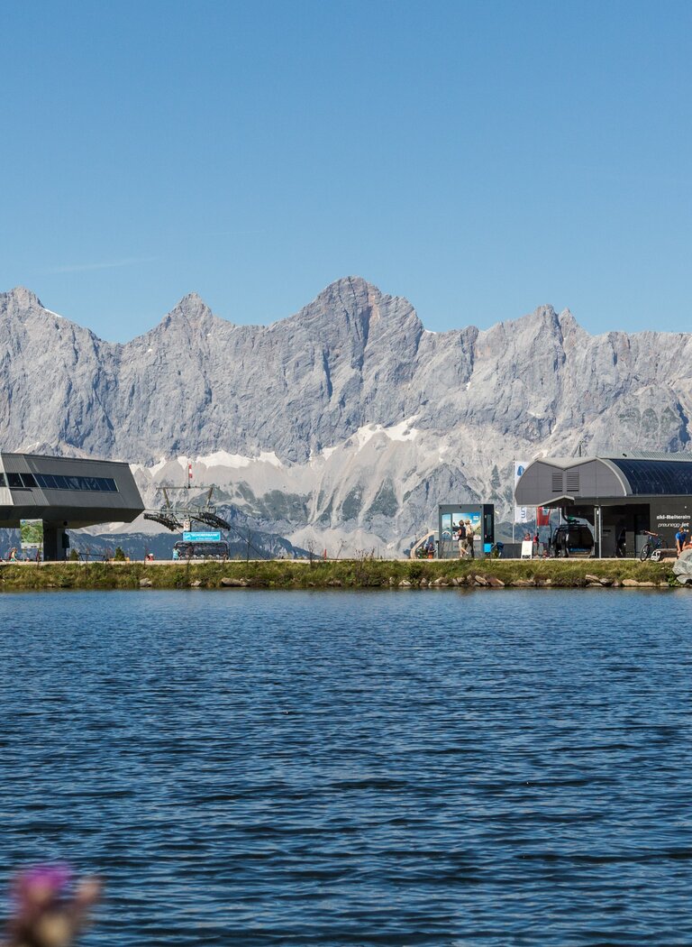 View across the reservoir to Reiteralm gondola station with majestic Dachstein range in the background. | © Reiteralm Bergbahnen GmbH & Co.KG