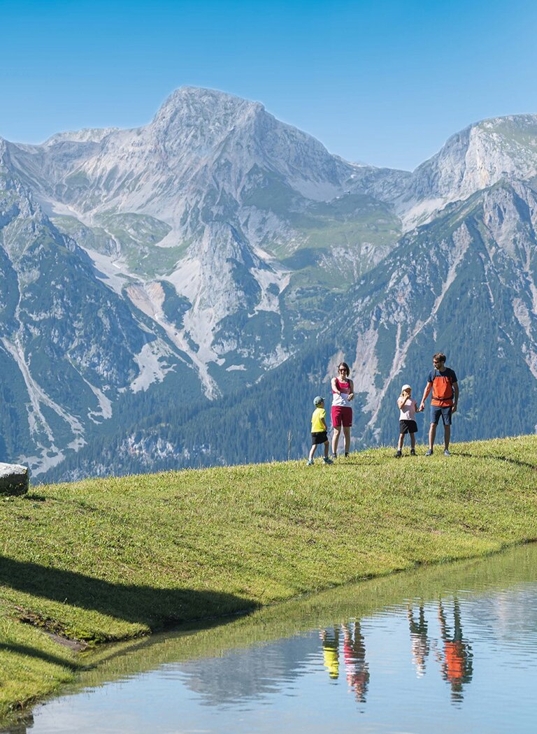 Family hiking by a clear lake with mountain panorama and water reflections. | © Ski amadé GmbH