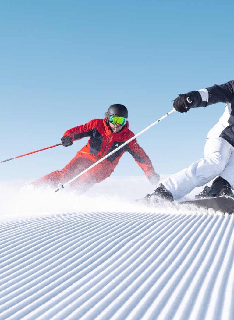 Zwei Skifahrer in sportlicher Haltung fahren nebeneinander über frisch präparierte Rillenpiste bei Sonnenschein in Ski amadé. | © Ski amadé GmbH